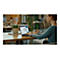 Frau am Laptop in einem CafÃ©; Diagramm auf dem Bildschirm. Vorne Pflanze, Person im Hintergrund.