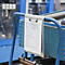 Klemmbrett mit einer Prüfliste hängt an einem blauen Metallwagen in einer Industriehalle.