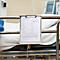 Klemmbrett mit Patienteninformationsblatt hängt am Metallgitter eines Krankenhausbetts.