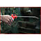 Eine Hand hält eine rote Druckluftpistole, die auf eine Maschine gerichtet ist. Metallspäne liegen daneben.