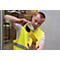A man is applying yellow warning tape to a yellow safety vest. He is holding the roll and the vest. In the background a warehouse.