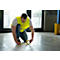 A man kneels and applies yellow tape to a concrete floor.