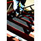 Person standing on metal stairs. The steps are red and black. The person is wearing jeans and brown shoes.