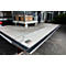 Loading ramp of a truck with a loaded trolley. Black edge protection, paved floor, person in the background.