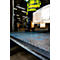 A worker in a yellow high-visibility overall pushes pallets into a warehouse. In the foreground, an anti-slip strip is visible on the floor.