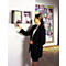 A woman in a black blazer points to an open wall book, an abstract painting hangs behind it.