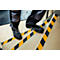 Person steps up stairs with yellow and black safety strips on the steps.