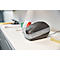 A label printer dispensing an address label sits on a white tabletop. Office supplies in the background.