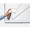 A hand spraying a cleaning agent onto a whiteboard with a diagram. The text on the bottle is readable.
