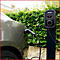 Graues Auto lädt an einer Ladestation. Schwarzes Kabel verbindet Auto und Ladestation. Im Hintergrund Hecke.