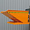 Orange Kippbehälter mit gelb-schwarzem Warnstreifen. An Gabelstapler montiert. Hintergrund: graue Metallfassade.