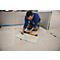 A man in blue work clothes kneels on a floor, drawing a line on a tile with a pencil. Next to him lie a level and a square.