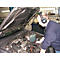 Ein Mechaniker mit Kopfhörern prüft einen Motorraum. Die Motorhaube ist geöffnet. Im Hintergrund Werkzeuge.