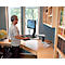 A man stands at a height-adjustable desk and works on the computer, looking left. The office is bright and furnished.