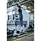 Un homme sur un escabeau monte une machine dans une usine. Escabeau gris, pantalon bleu.