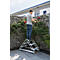 Homme debout sur un escabeau, coupant des roses devant des gabions en pierre. Maison en arrière-plan.