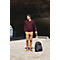 Ein Mann in weinrotem Pullover und beigefarbener Hose steht mit Rollkoffer. Er blickt zur Seite.