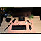 Schreibtisch mit Monitor, Tastatur, Uhr, Handy, Lampe und Maus. Rosa Matte, helles Holz. Alles ist ordentlich angeordnet.