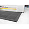 Black workstation mat with rounded edges and hole pattern. It lies in front of a machine on a white floor.