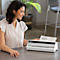 A smiling woman laminates a sheet with the word "GOALS". A white laminator is on the table.
