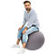 A man in a striped shirt and jeans sits on a gray exercise ball. He is looking at the camera.