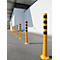 Line of yellow bollards with black stripes. On asphalt in front of a white wall, a facade with a roof on the left.
