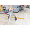 Shopping cart filled with groceries stands in front of a checkout counter. Yellow line on the floor marks distance.