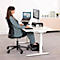 Eine Frau sitzt an einem weißen höhenverstellbaren Schreibtisch und arbeitet mit einem Laptop und einem Monitor. Sie hat eine ergonomische Körperhaltung.