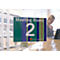 Ein Schild mit der Aufschrift "Meeting Room 2". Im Hintergrund eine Frau an einem Schreibtisch.