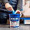 Eine Person entnimmt ein blaues Reinigungstuch aus einem blauen Eimer. Auf dem Eimer steht: SCRUBS IN-A-BUCKET HAND CLEANER TOWELS.