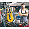 Ein Mechaniker steht in einer Werkstatt vor einem Eimer mit Reinigungstüchern, die Arme verschränkt. Er lächelt in die Kamera.