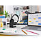 Black headset on a charging stand in front of a laptop showing a calendar. Pens and notes are on the table.