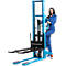 A woman stands next to a blue forklift and holds onto the handle.