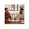 Deux personnes regardent des documents ensemble Ã  une table. Une femme en chemise rouge, un homme en pull beige.