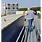 A man cleaning the roof of a blue trailer with a broom and a work platform.