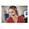 Eine lÃ¤chelnde Frau mit Headset spricht vor einem Computer. Sie trÃ¤gt ein orangefarbenes Hemd.
