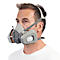 Un homme portant un masque respiratoire, parties grises, sangles autour de la tête et du cou, t-shirt blanc.
