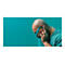 Un homme chauve portant un casque et des lunettes de soleil bleus touche son oreille, fond turquoise.