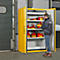 Un homme se tient près d'une armoire jaune. L'armoire contient des bidons rouges. Il sort un bidon de l'armoire.