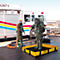 Deux personnes en combinaisons de protection sur une surface noire. Un camion de pompiers en arrière-plan, une personne avec un tuyau.