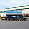 Tankwagen op een aanhanger met blauw chassis voor een fabriek, blauwe lucht en bomen.