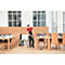 A waitress vacuums the floor in a restaurant, surrounded by tables, chairs, and windows.