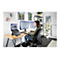 Une femme travaille Ã  un bureau avec deux moniteurs et un ordinateur portable. Elle porte un casque et est assise sur une chaise ergonomique.