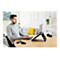 Homme sur ordinateur portable dans un salon. Il tape sur un clavier, l'ordinateur portable est sur un support. Souris et repose-poignet sur la table.