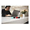 Trois clés USB (vert menthe, noir, rouge) sont posées sur une table. En arrière-plan, une personne est assise devant un ordinateur portable.