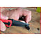 Nahaufnahme einer Hand, die ein rotes Taschenmesser benutzt, um einen schwarzen Ring zu schneiden. Der Hintergrund ist unscharf.