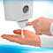 A person presses a soap dispenser with their finger, dispensing pink soap into their palm.
