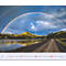 Un double arc-en-ciel surplombe un paysage avec un lac, des collines et une route.