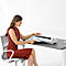 A woman sitting at a desk laminates documents. She wears a rust-colored dress and smiles.