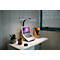 Bureau avec ordinateur portable, lampe et plante. Une lampe de lecture noire éclaire le cahier. À droite une fenêtre, à gauche une plante en pot.